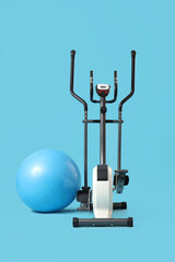 Modern exercising bike with fitball on blue background
