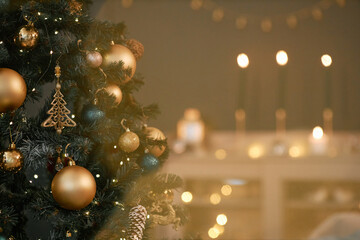 Christmas tree decorated with gold and green ornaments standing in foreground, glowing string...