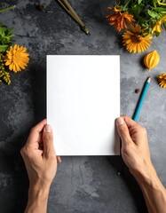 Hands holding blank paper surrounded by blooms and writing supplies