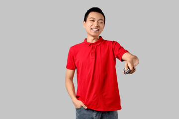 Fototapeta premium Young Asian man with remote controller watching TV on grey background