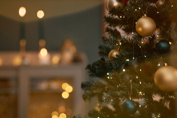 Christmas tree decorated with gold and dark ornaments standing indoors with string lights glowing,...