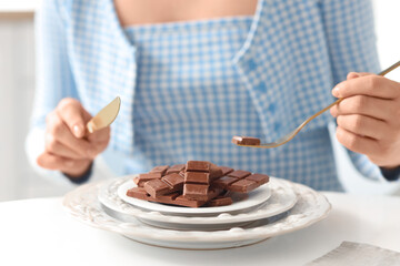Young woman eating tasty chocolate at table in kitchen, closeup