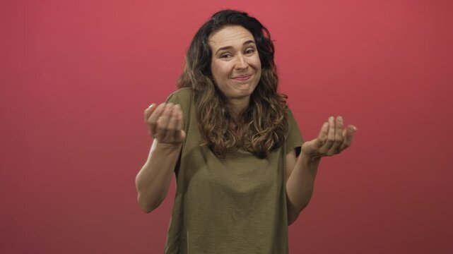 Woman in olive shirt shrugs arms with raised shoulders in studio with red background; quiet uncertainty.