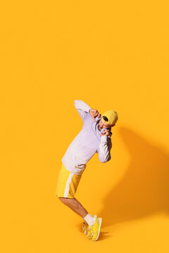 Handsome young man in headphones dancing hip-hop on orange background