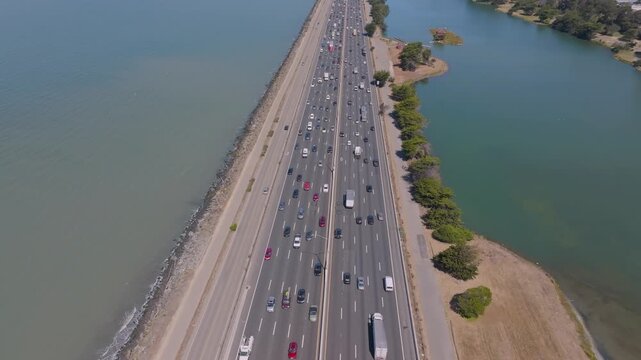 4K aerial drone footage of Interstate 880 near Berkeley Aquatic Park in Berkeley, California, showing dense car traffic moving slowly during peak commute hours. Multiple lanes are full, with the shore