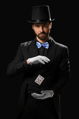 Male magician with levitating playing card on dark background
