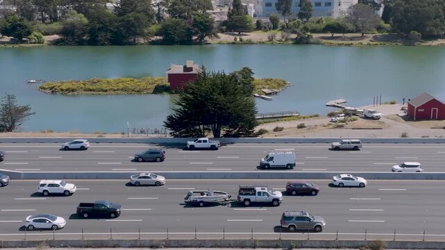 4K aerial drone footage of Interstate 880 near Berkeley Aquatic Park in Berkeley, California, showing dense car traffic moving slowly during peak commute hours. Multiple lanes are full, with the shore
