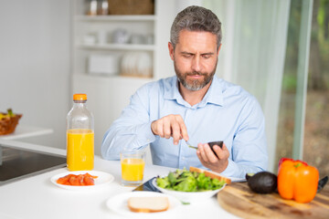 Healthy nutrition mature man. Aged man with healthy products at kitchen. Handsome 50s Senior Man Eating Tasty Meal In Kitchen At Home. Elderly Man at Table Enjoying Delicious Food. Morning breakfast.