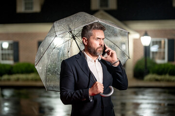 Night business. Businessman talks on his phone under an umbrella on a rainy night. Manager makes a...
