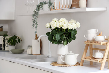 Vase with white roses and teapot on counter in kitchen