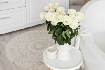 Vase with white roses on table in bathroom