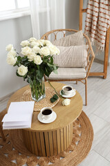 Vase with white roses, cups of coffee and book on table in living room