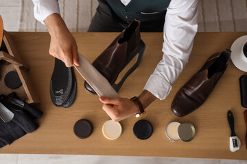 Male shoemaker polishing leather boot at table in workshop, top view