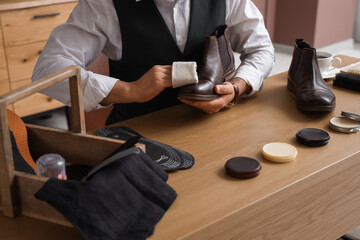Male shoemaker polishing leather boot at table in workshop