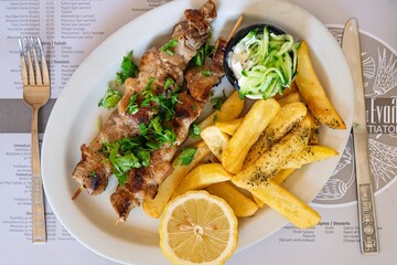 Enjoy authentic Greek souvlaki skewers paired with crispy fries, a zesty lemon wedge, and rich tzatziki sauce. A perfect dish for food lovers and culinary enthusiasts.