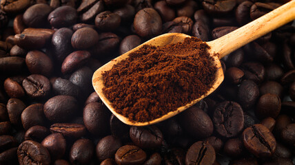 Background of coffee beans on which there are coffee grounds in a wooden spoon
