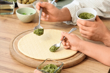 Father with his little daughter applying pesto sauce on pizza dough in kitchen, closeup