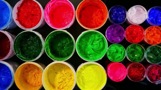 A collection of plastisol inks stored in sturdy barrels and glass jars, each filled with rich and vibrant colors red, blue, yellow, green, pink, orange, purple, and white in screen printing factory