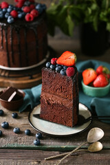 Cut sweet chocolate cake with fresh berries on wooden table