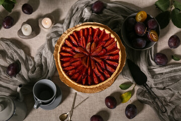 Wooden stand with tasty plum pie, teapot, cups and spatula on table