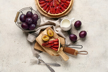 Tasty plum pie with spatula, fresh fruits and jug of milk on light background