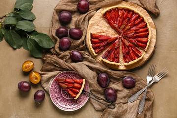 Tasty plum pie with spatula, fresh fruits and leaves on brown background