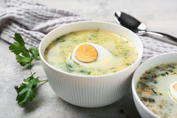 Bowl of tasty green borscht with parsley and spoon on grey grunge background