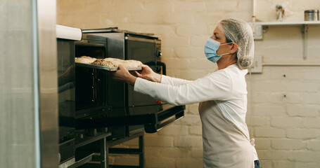 Bakery, woman and donuts in oven in kitchen for breakfast order, baking process and catering service. Hospitality industry, baker and mask in small business for dessert preparation and pastry snack