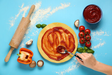 Female hand, ingredients and pizza dough with tasty tomato sauce on blue background