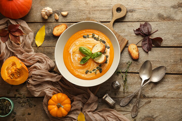 Bowl of tasty pumpkin cream soup with seeds, croutons, basil and thyme sprigs on wooden background
