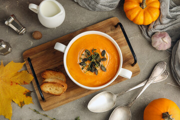 Pot of delicious pumpkin cream soup with seeds and herbs on grey grunge background