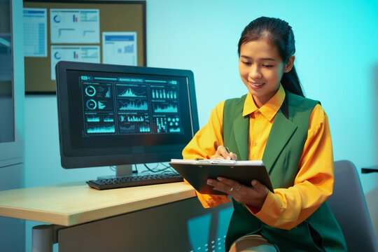 An Asian businesswoman analyzes digital charts on a computer screen, reviewing performance reports and financial data to develop strategic business insights and support decision-making in a modern