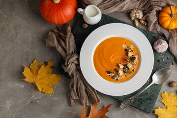 Plate of tasty pumpkin cream soup and ingredients on grey grunge background