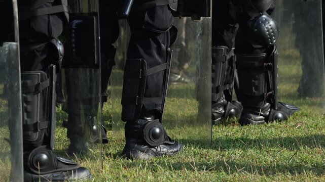 Legs of Anti-riot squad. Heavily armored special police forces create barricade on the street. Close up of boots. Tactical armed policeman on protest. Riot police team in black uniform. Demonstration
