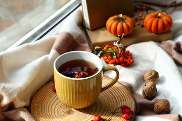 Mug of tasty rose hip tea and autumn decor on windowsill in living room, closeup