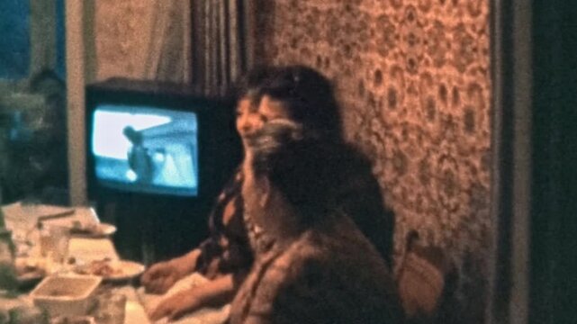 Cheerful adult daughter communicates with elderly mother at dinner table in family circle in apartment. Woman express feelings. Generation meeting near TV. Vintage film. Retro archive 1980s Ukraine