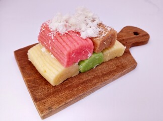 Gethuk lindri, a colorful traditional Indonesian cake made from rice flour, neatly arranged on a wooden board. Each piece is topped with grated coconut, creating a sweet and appetizing appearance