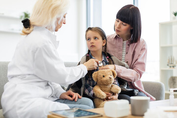 A female doctor uses a stethoscope to listen to a young girl's heart while her mother comforts her....