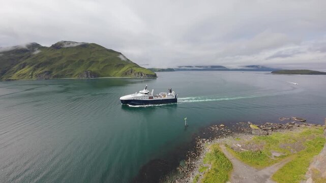 Aerial view of factory trawler and mountain coastline in Unalaska, Alaska. Commercial fishing in Bering Sea, Alaska, USA. Fishing vessel moving through clear water in Dutch Harbor