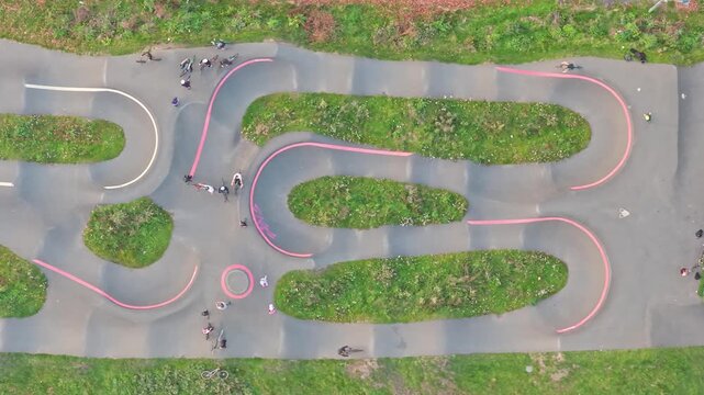 Top down static drone shot displays BMX freestyle riders flowing around the winding pump track in Hillsborough Park, Sheffield, South Yorkshire, England, highlighting curves, movement, and community