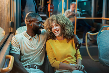 Interracial couple laughing and traveling on public bus at night