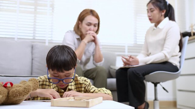 Therapy, child, counseling, parent, consultation as mother expresses worry in clinical setting, therapist offers gentle support while boy plays quietly, difficult parenting moment addressed