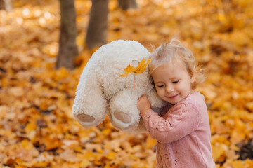 Cute girl hugging a teddy bear in autumn foliage.