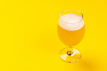 A frothy glass of fresh beer against a bright yellow background