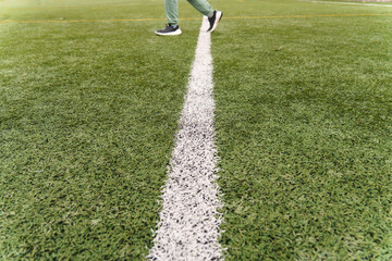 Person walking across a white line on a green artificial turf soccer field, representing progress or boundaries 