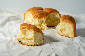 orn pieces of a soft, golden-brown bread roll are resting on a rumpled white cloth, revealing the fluffy interior texture against a plain white background.