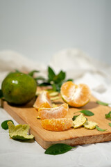 Peeled orange segments are stacked on a wooden cutting board. Green peels, leaves, and a halved orange are scattered nearby, with a shallow depth of field.