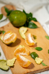 A high-angle, vertical shot of peeled green-skinned oranges, with segments and peel scattered on a light wooden cutting board on a white cloth.