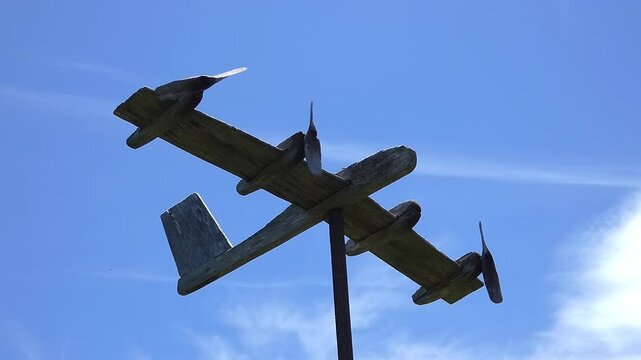 Close-up of an old handcrafted wooden decorative airplane weather vane with spinning propellers and gentle movement in the wind. Rustic handmade craftsmanship and vintage charm