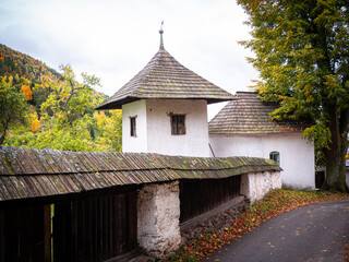 Historic churchyard wall and white tower with wooden shingle roof in Špania Dolina, Slovakia, surrounded by autumn trees and mountains. © Marek